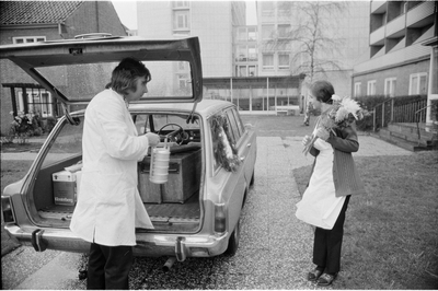 Ein Mann reicht einer Frau aus einem Auto ein Behältnis mit warmem Essen