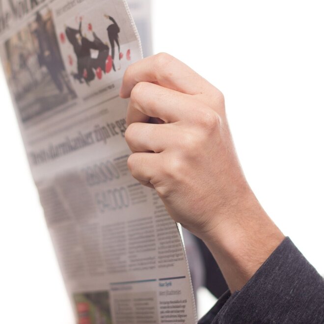 zwei Hände halten eine geöffnete Zeitung zum Lesen